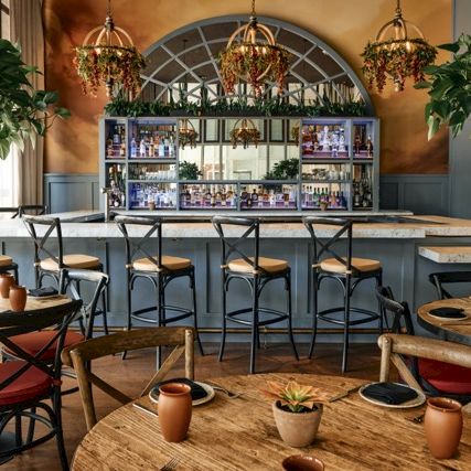 A cozy rustic kitchen with a brick oven, wooden shelves, copper pots, and a warm, inviting dining area bathed in natural light.
