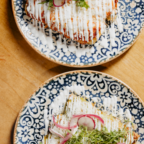 Two plates of fancy, plated dishes with grilled meat, herbs, and a light sauce; a wooden table backdrop. Top it at 140 characters, always ending the sentence.