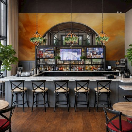 A stylish caf&eacute; interior with a long wooden bar, metal stools, shelves of bottles, warm lighting, and a curved hanging rack behind the counter. Top it at 140 characters, always ending the sentence.