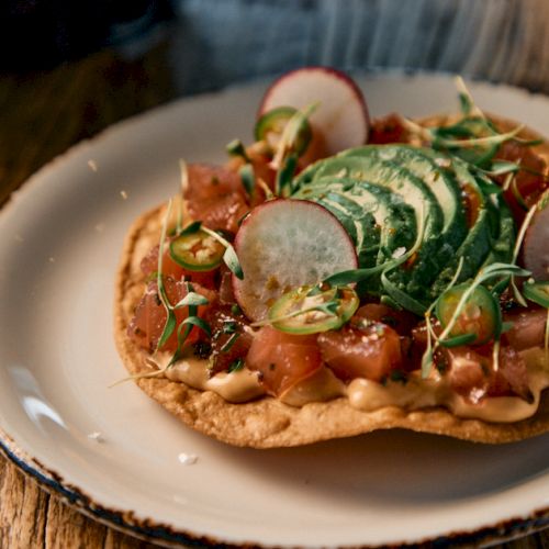 A plate with tacos or quesadillas topped with greens and lime wedges, served on a colorful, tiled table.