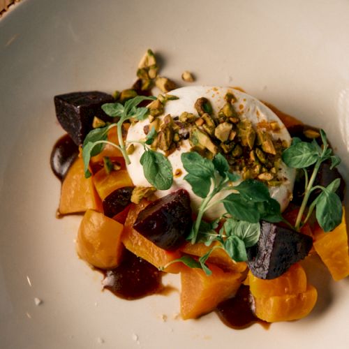 A plated dish with a protein and greens, drizzled sauce, on a round white plate with a dark rim.