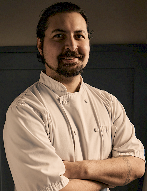 A chef in a white double-breasted jacket stands proudly with arms crossed, confident and ready to create.