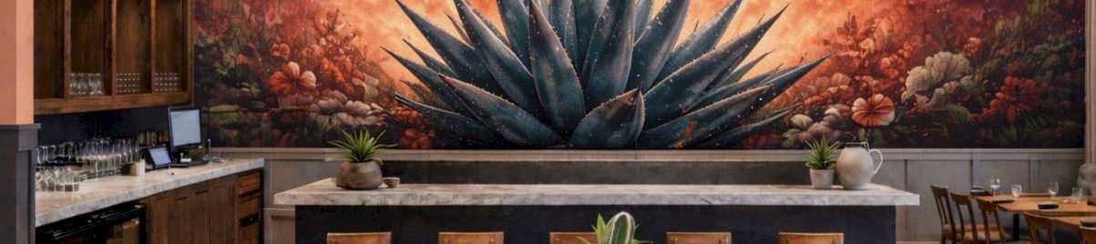 A cozy restaurant interior with a dramatic mural of a large agave plant against a red moon sky, warm wood tables, plants, and soft lighting.