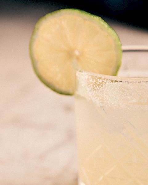 A glass of light-colored drink with a lime wedge garnishing the rim, on a light countertop, bright and refreshing.