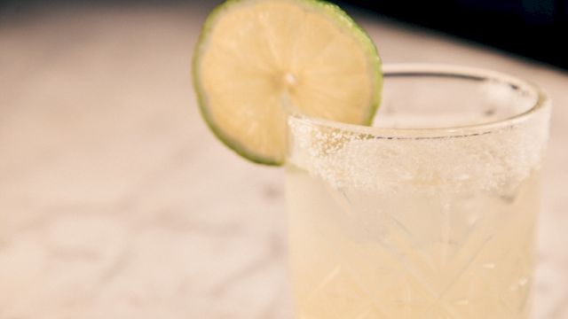 A glass of light-colored drink with a lime wedge garnishing the rim, on a light countertop, bright and refreshing.