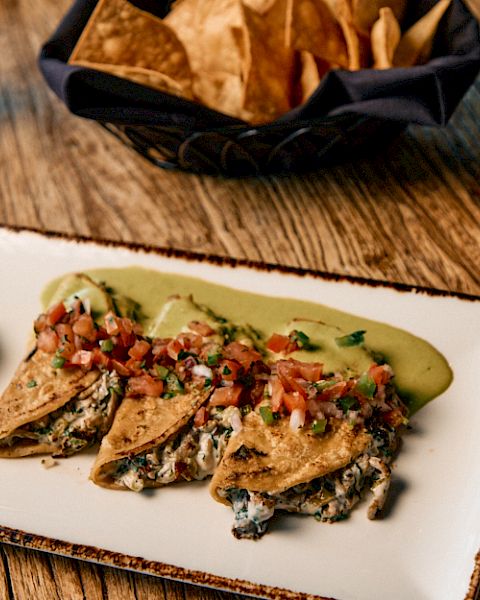 Crispy fish tacos with salsa, lime wedge, roasted corn tortilla chips, and a mug of coffee on a rustic wooden table.