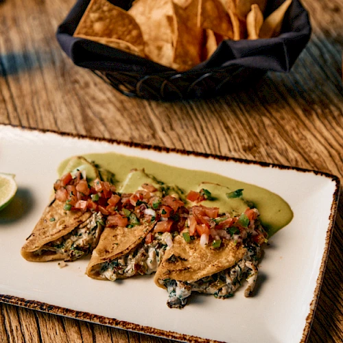 Crispy fish tacos with salsa, lime wedge, roasted corn tortilla chips, and a mug of coffee on a rustic wooden table.
