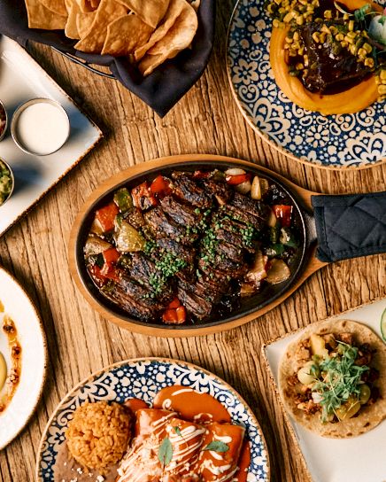 A vibrant table of tapas and small plates: sizzling skillet, bowls, and bite-sized tacos arranged on rustic wooden table.