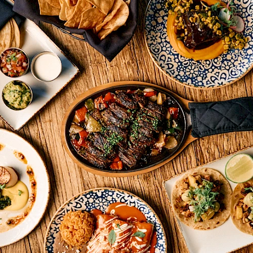 A vibrant table of tapas and small plates: sizzling skillet, bowls, and bite-sized tacos arranged on rustic wooden table.
