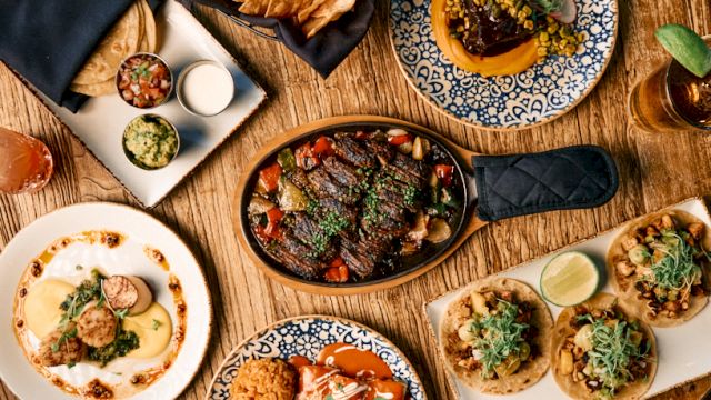 A vibrant table of tapas and small plates: sizzling skillet, bowls, and bite-sized tacos arranged on rustic wooden table.