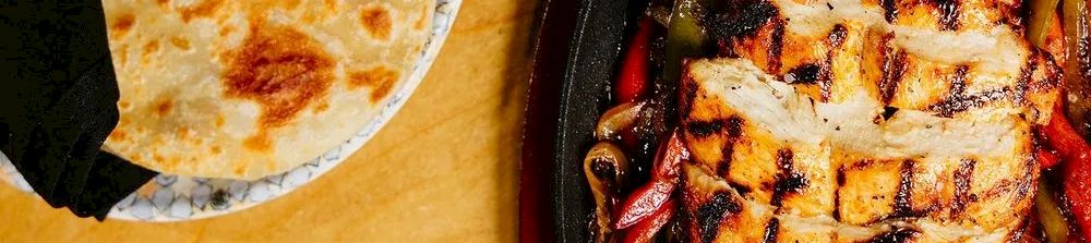 Sizzling grilled chicken with veggies on a skillet beside warm naan bread—delicious, colorful, and ready to share.