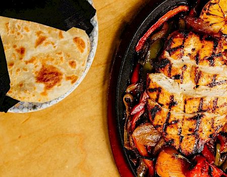 Sizzling grilled chicken with veggies on a skillet beside warm naan bread&mdash;delicious, colorful, and ready to share.