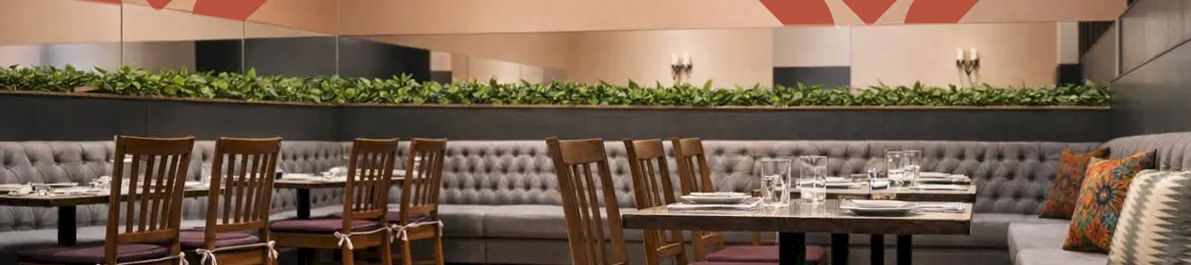 A stylish restaurant interior with warm wood floors, wooden chairs, cushioned seating along the wall, and pink geometric tree-like wall decals.