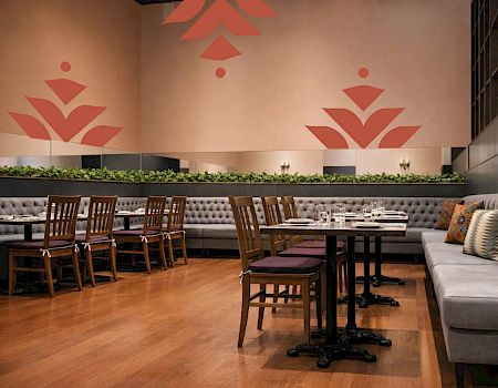 A stylish restaurant interior with warm wood floors, wooden chairs, cushioned seating along the wall, and pink geometric tree-like wall decals.