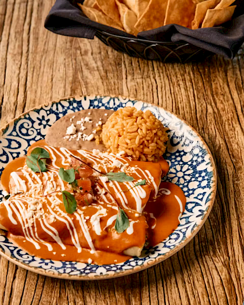 A plate of orange-sauced dumplings with rice and basil sits on a wooden table beside forks, knife, and a napkin.